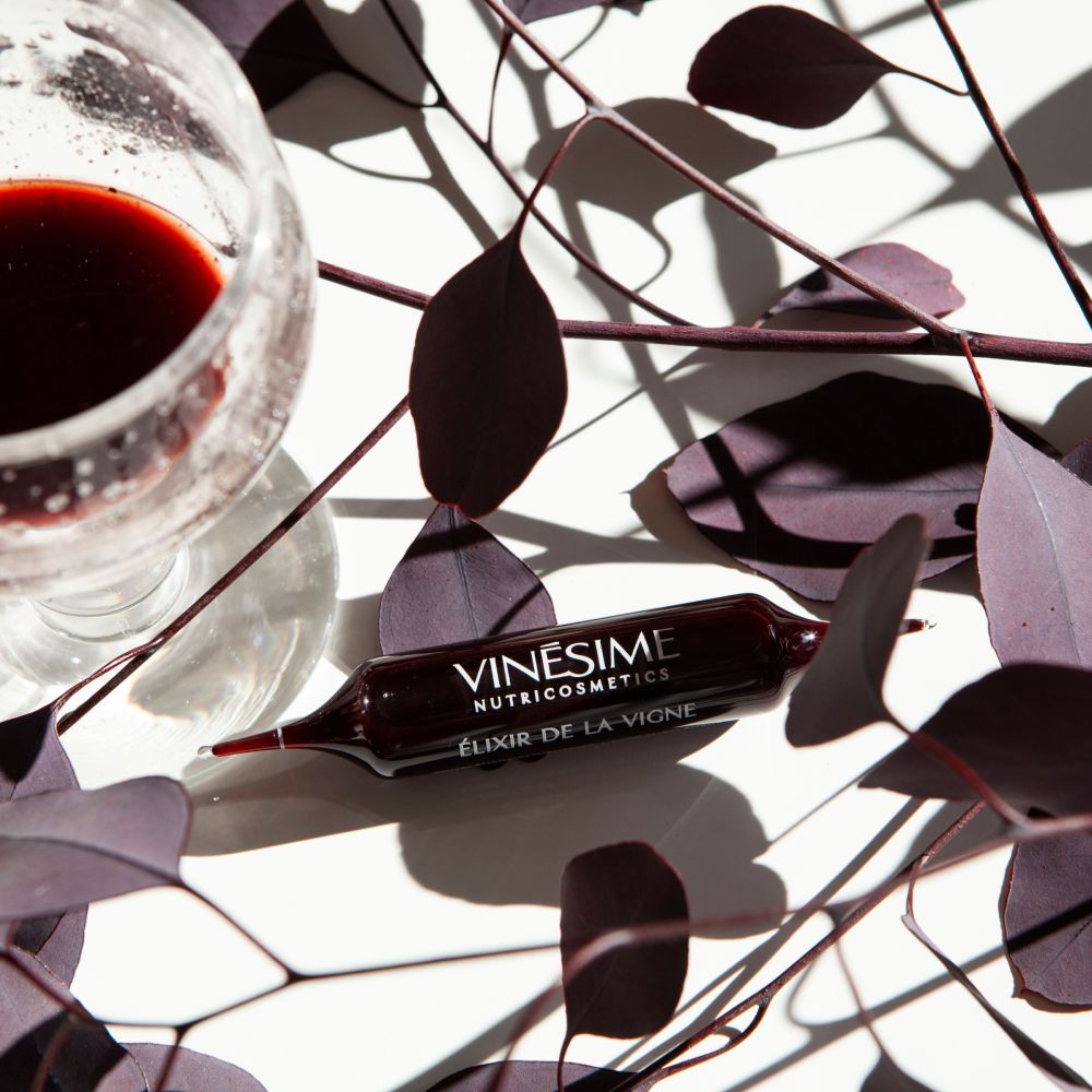 ampoule vinesime elixir de la vigne cure nutricosmetique pinot noir avec des feuilles et et un verre à pied
